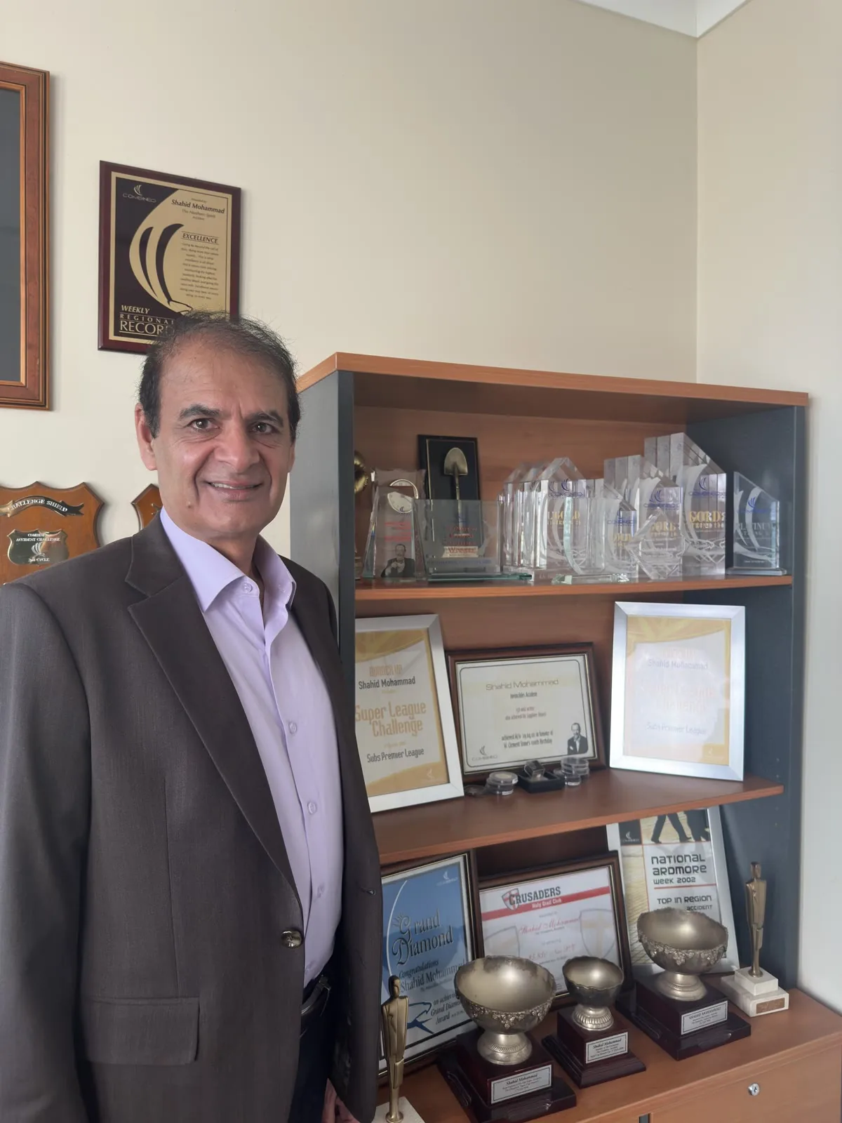 Shahid Mohammad standing beside his industry awards at the Insurance Time office.